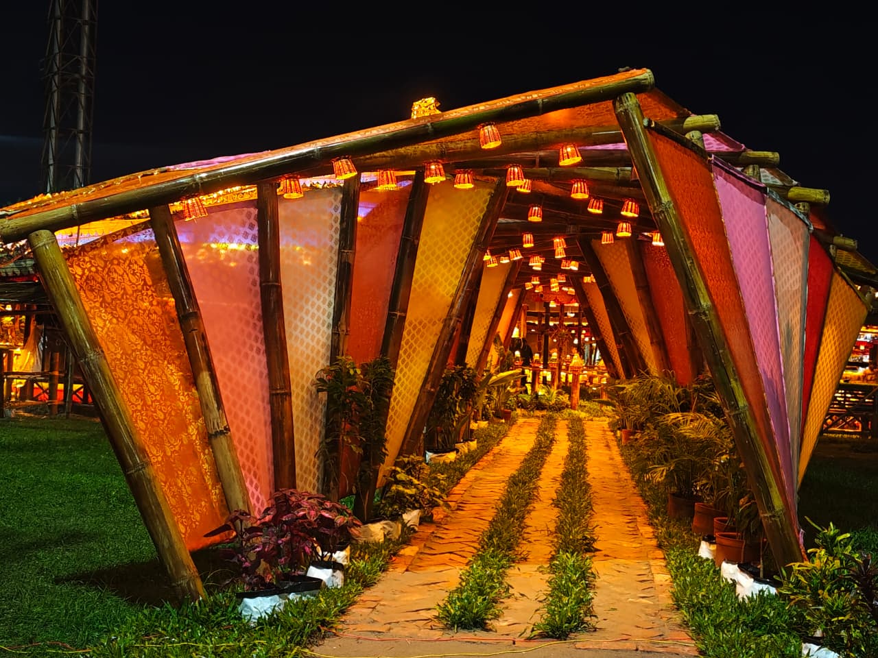 A stunning bamboo tunnel entrance with fabric panels and brick pathway, lit at night