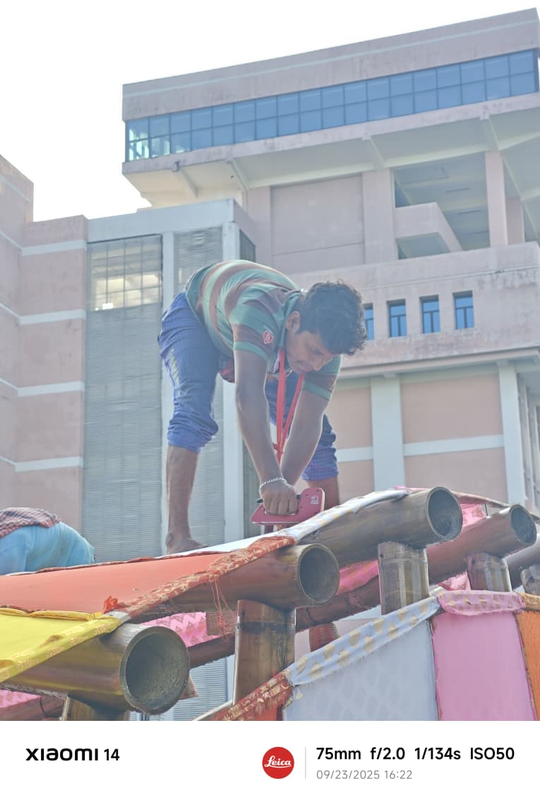 A karigar wrapping fabric on bamboo roof with IIT KGP building in background